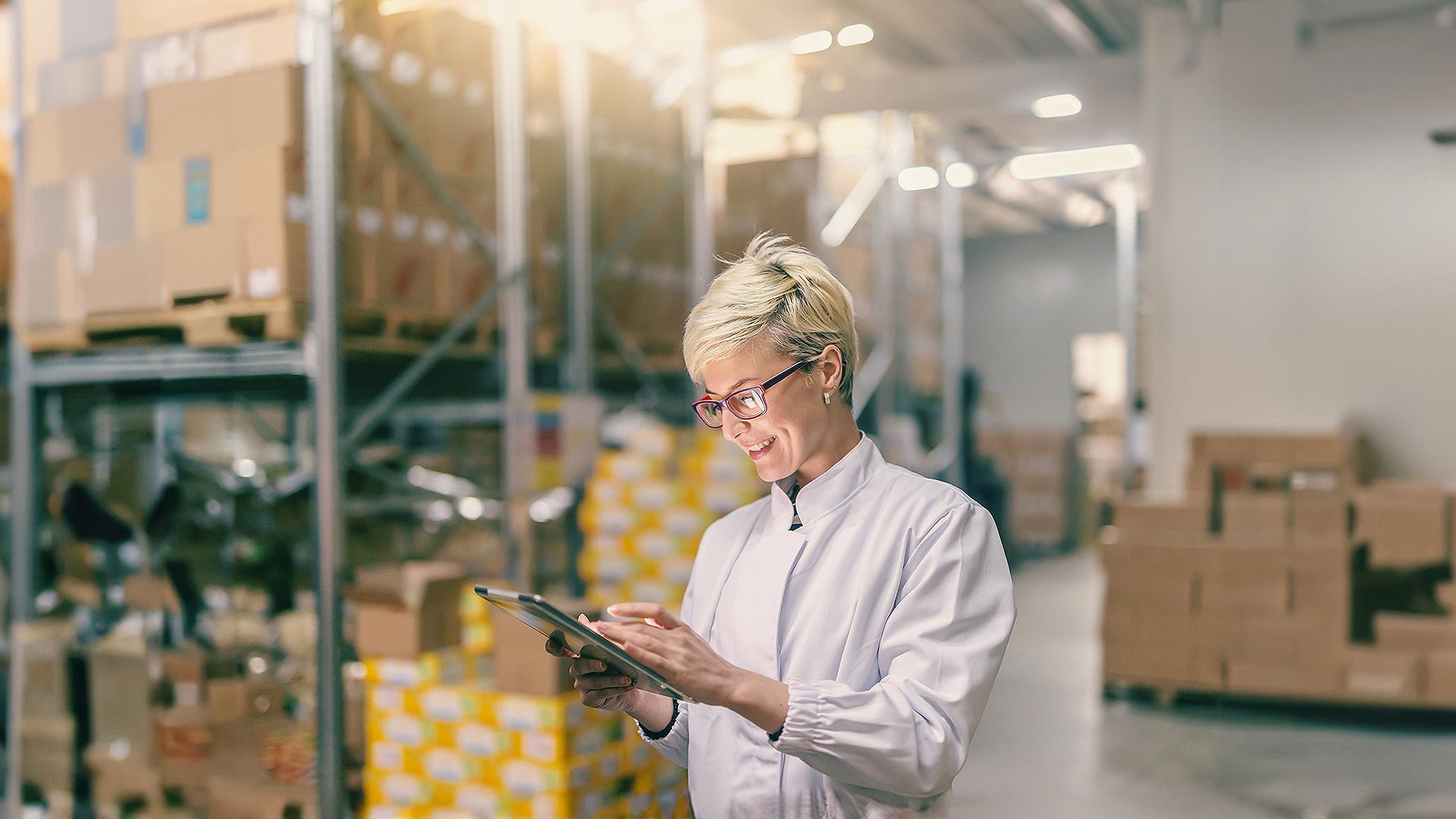 A smiling woman against the background of a magazine with shipments, looking at the tablet, holding in her hand.
