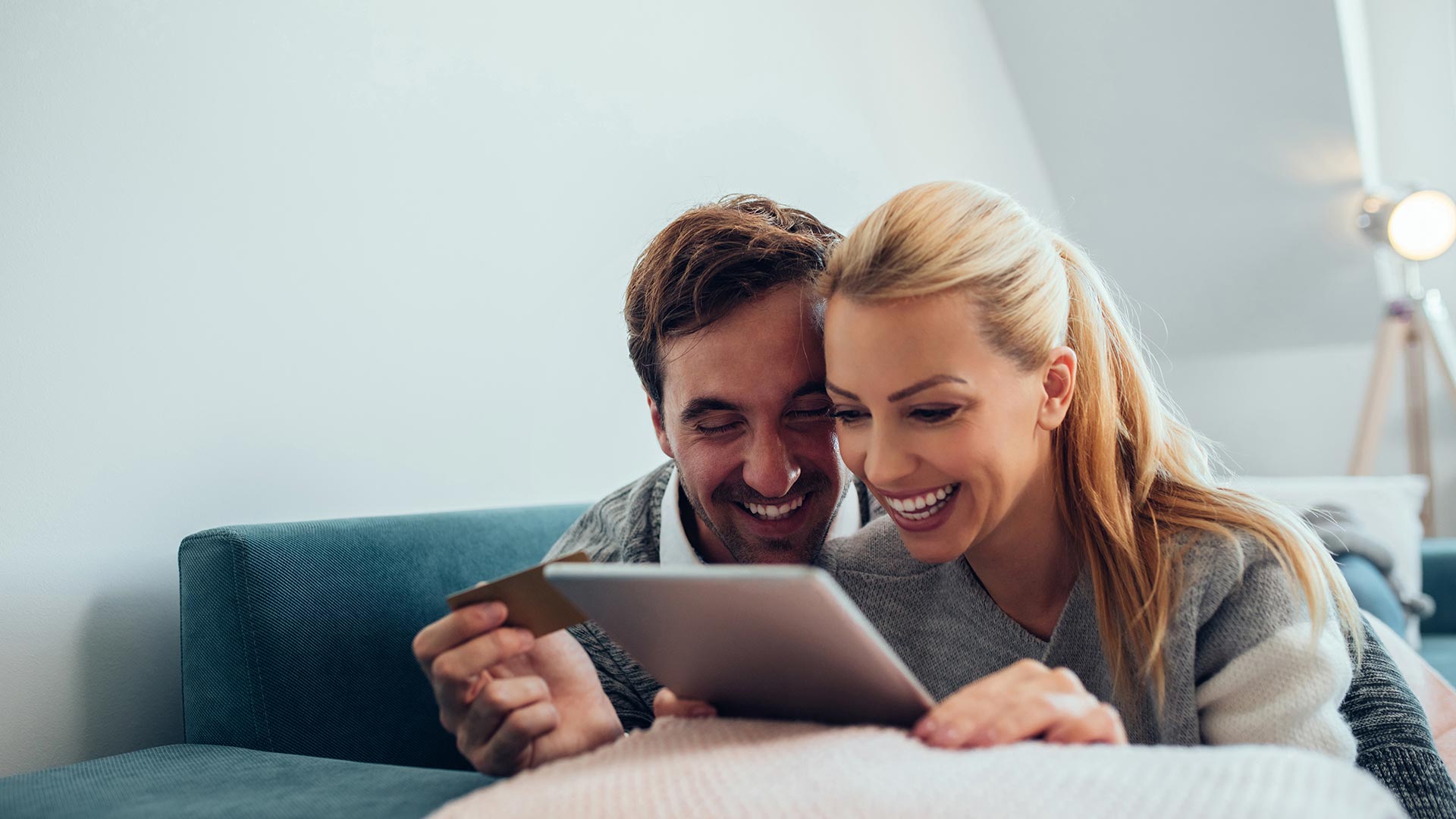 A smiling woman and a man, against a bright room, looking at the tablet that a woman holds in her hand