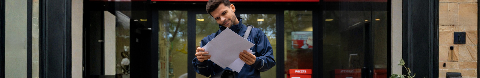 listonosz przed placówką pocztową przeglada listy